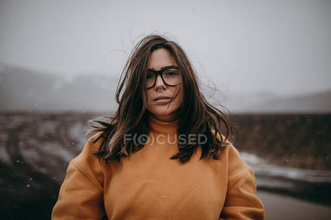 Young happy tourist in eyeglasses with piercing looking at camera between deserted ground in snow — Stock Photo