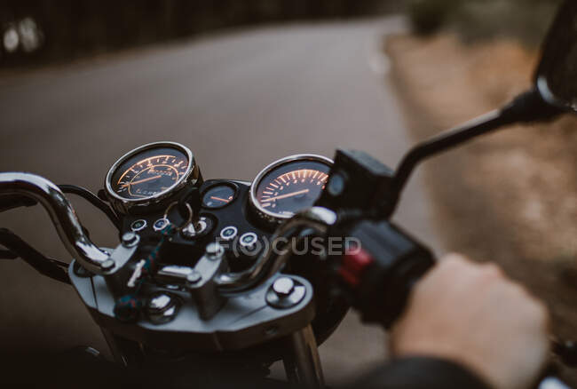 Person crop driving on motorcycle on asphalt route between forest — Stock Photo