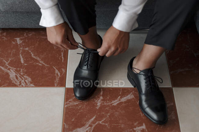 From above crop anonymous gentleman in white shirt tying shoelaces on classy black leather shoes — Stock Photo