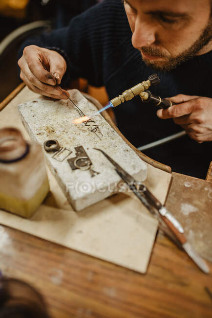 Бородатый мужчина ювелир, используя щипцы, делая крошечные металлические детали на верстаке в мастерской — стоковое фото