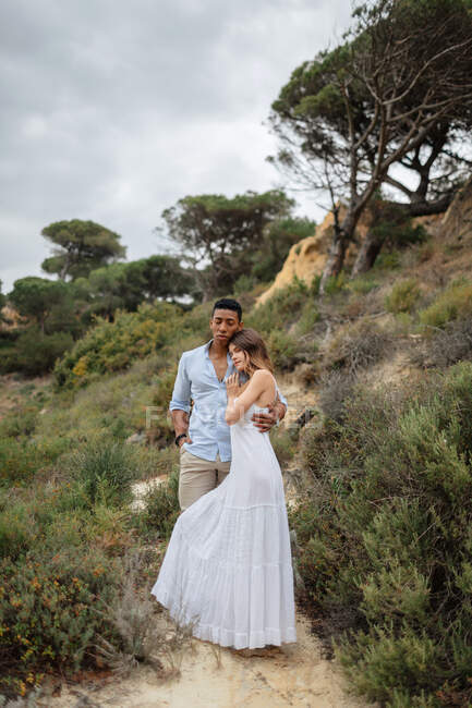 Разнообразные обнимающие невесту и жениха, стоя в лесу в день свадьбы — стоковое фото