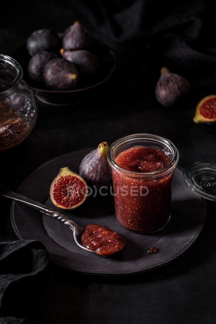 Von oben frische Fruchtmarmelade in kleinem Glas und auf Löffel mit vollen und geschnittenen Feigen auf Teller am schwarzen Küchentisch — Stockfoto