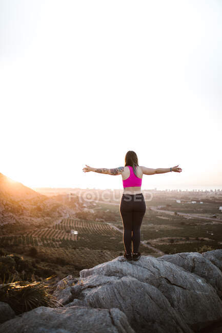 Picturesque view of young tourist standing on peak of mountain and looking away in sunny day — Stock Photo