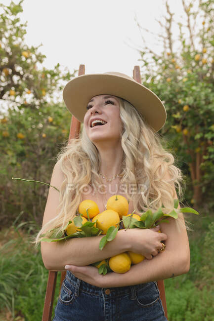 Positives Weibchen mit geöffnetem Mund steht während der Erntezeit mit Zitrusfrüchten in der Hand im Obstgarten — Stockfoto
