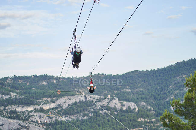 Pessoas corajosas anônimas em equipamentos de segurança montando tirolesa sobre montanhas no verão — Fotografia de Stock