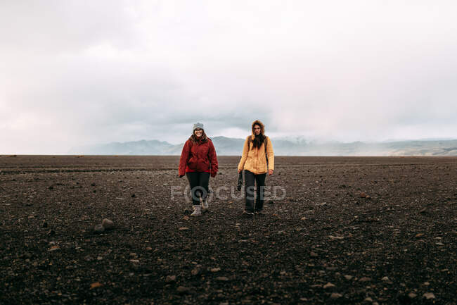 Молодые счастливые туристы в зимней одежде ходят по безлюдной земле и облачному небу — стоковое фото