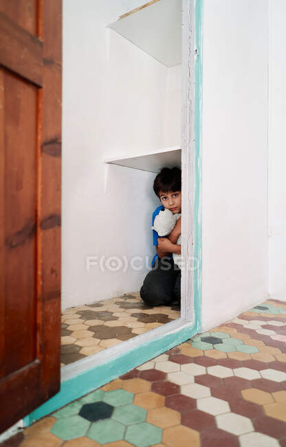 Infeliz niño asustado con juguete escondido en el armario mientras sufre de violencia doméstica - foto de stock