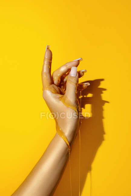 Врожай невизначена жінка, що демонструє руку з манікюром та ароматичними медовими рідинами на жовтому тлі з відтінком — стокове фото