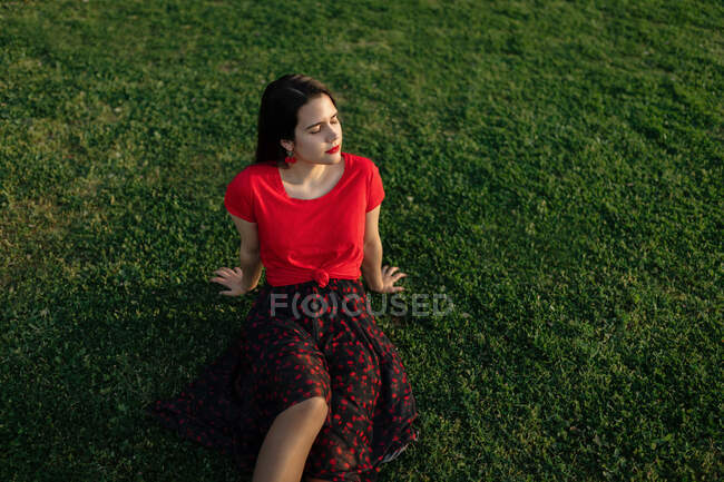 Femme tranquille assise sur l'herbe sur la prairie dans le parc et profiter du coucher du soleil en été — Photo de stock