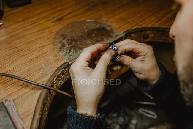 Anónimo joyero sosteniendo anillo inacabado en manos sucias y comprobando la calidad en el taller - foto de stock