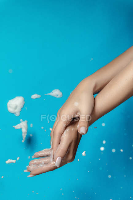 Анонимная женщина с длинными ногтями, демонстрирующая руки с белой пеной на синем фоне — стоковое фото