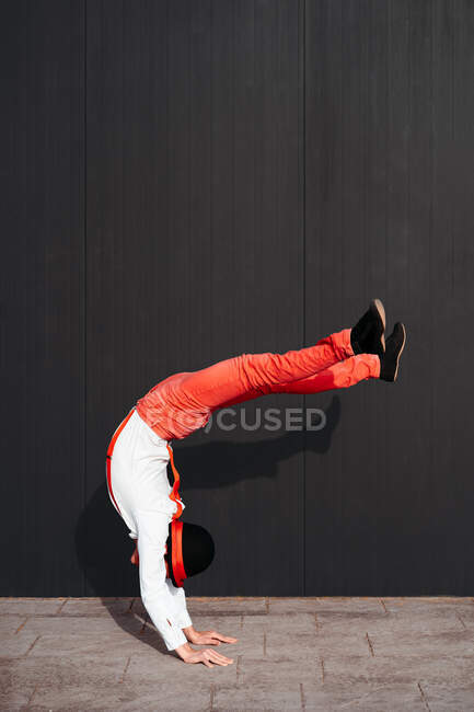 Вид збоку на невпізнаваного гнучкого виконавця циркового цирку, який робить сором'язливий трюк проти чорної стіни — стокове фото