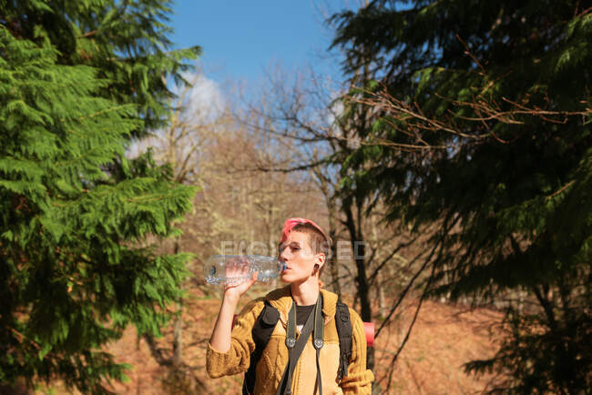 Жадаюча жінка мандрівник з рюкзаком насолоджується прісною водою в сонячний день на природі — стокове фото