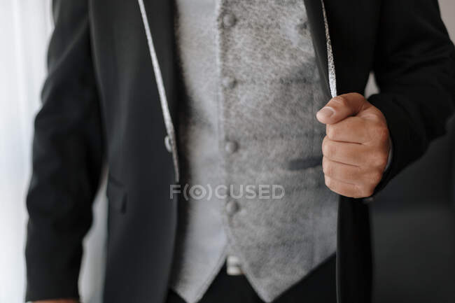 Crop novio anónimo usando elegante traje negro con clase con chaleco gris vestido para la ceremonia de boda - foto de stock