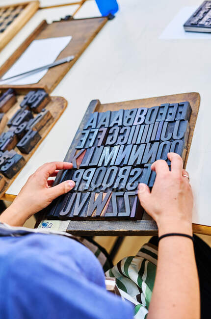 D'en haut de travailleur masculin anonyme travaillant avec alphabet letterpress sur planche en bois dans l'atelier — Photo de stock