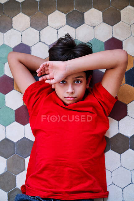 De cima de infeliz menino pré-adolescente solitário deitado no chão como vítima de violência doméstica e abuso olhando para a câmera — Fotografia de Stock