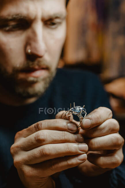 Joalheiro segurando anel inacabado em mãos sujas e verificando a qualidade na oficina — Fotografia de Stock
