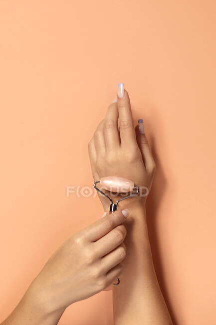 Ritaglio anonimo femminile dimostrando rullo di quarzo rosa per il trattamento della pelle facciale e massaggio su sfondo beige — Foto stock