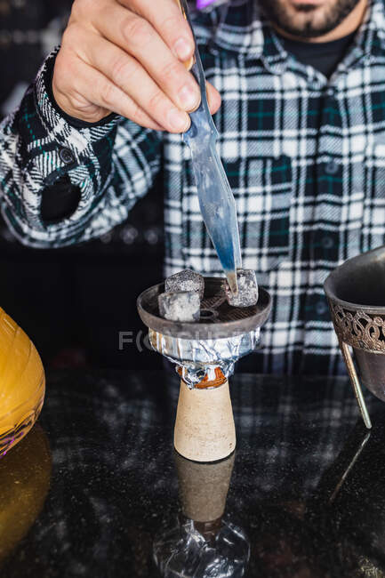 Zugeschnittener, bis zur Unkenntlichkeit männlicher Barkeeper bereitet Schüssel mit Holzkohle für Wasserpfeife in einem Nachtclub vor — Stockfoto