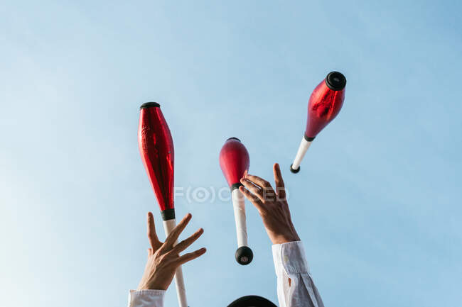 Знизу врожаю анонімний цирк художник виконує трюк з жонглювання клубів проти блакитного неба — стокове фото