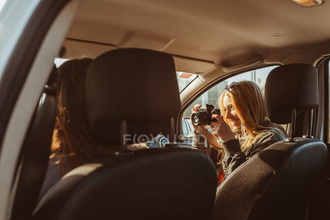 Frau mit Oldtimer-Kamera fotografiert Freundin beim Autofahren bei sonnigem Tag — Stockfoto