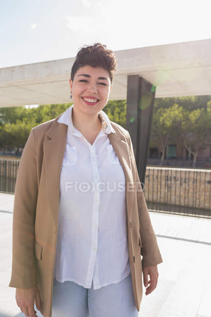 Happy young female in trendy clothes standing on walkway in city looking at camera in sunny summer day — Stock Photo