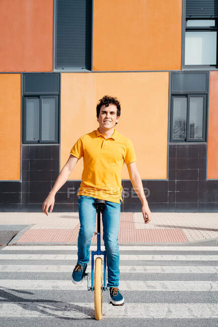Homem talentoso em desgaste casual sentado na estrada de passagem de monociclo na zebra na rua urbana moderna com edifício colorido — Fotografia de Stock