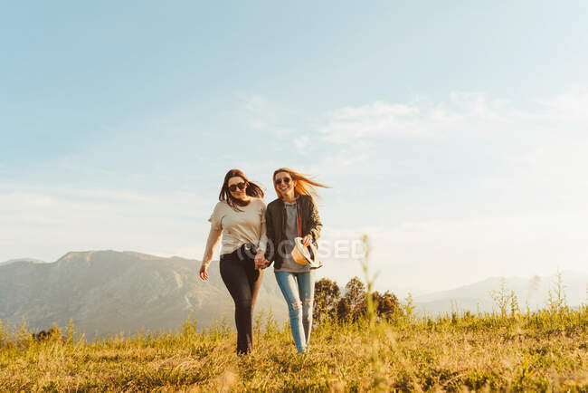 Lachende Frauen, die gemeinsam im Sonnenlicht auf der grünen Wiese im Gebirgstal spazieren — Stockfoto