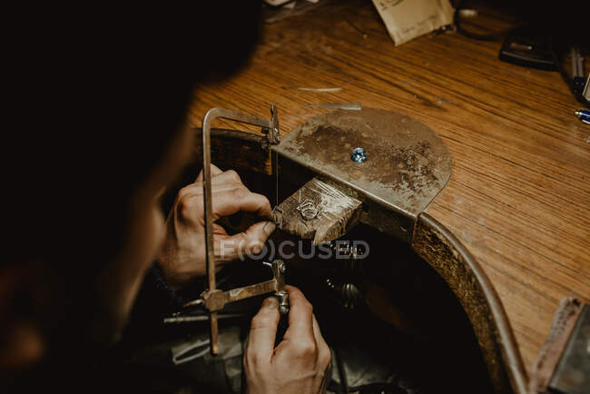 Goldsmith cutting metal with saw while making jewellery in workshop — Stock Photo