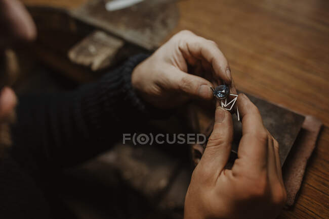 Orafo irriconoscibile che tiene gemma e ornamento di metallo sul tavolo mentre fa anello in officina — Foto stock