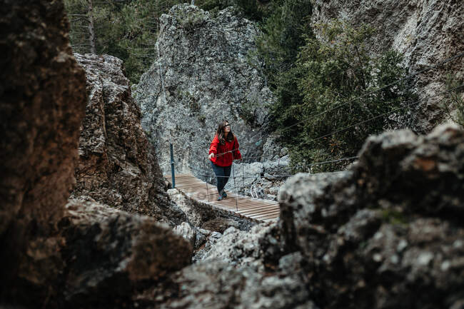 Вид на молодого туриста с рюкзаком, идущего по дорожке над водой возле каменной стены между лесом — стоковое фото