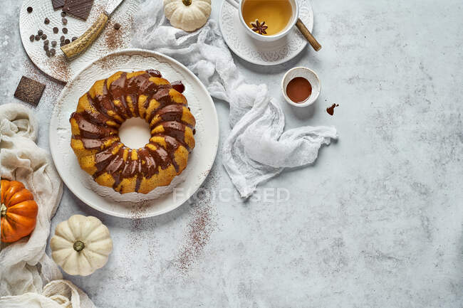From above autumn breakfast composition with homemade round cruller with chocolate topping cup of warm drink and little pumpkins on white background — Stock Photo