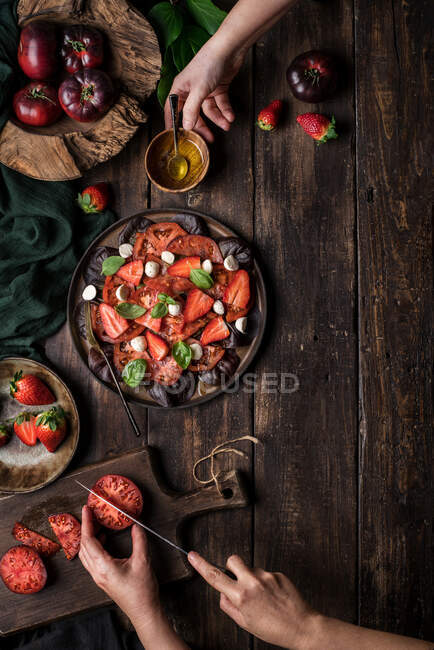 Anonymous people preparing a healthy tomato and strawberry salad on a wooden rustic table — Stock Photo