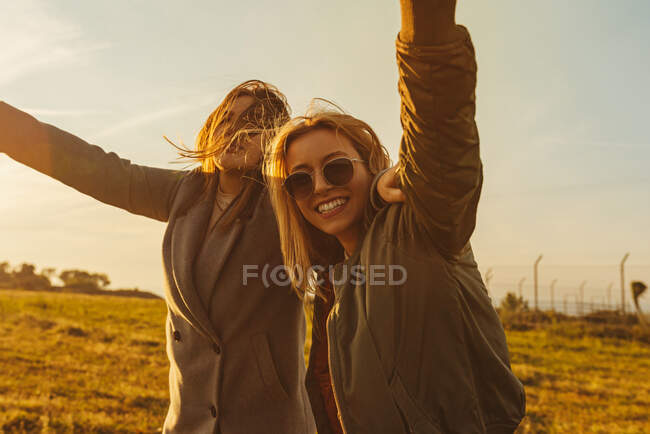 Mujeres alegres con velas brillantes abrazándose en el prado en las montañas divirtiéndose al atardecer - foto de stock