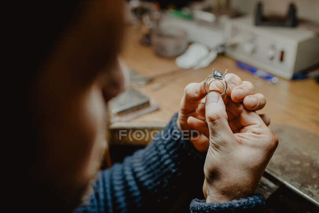 Bijoutier anonyme tenant la bague inachevée dans des mains sales et vérifiant la qualité dans l'atelier — Photo de stock