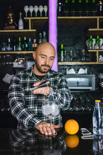 Barman masculin concentré ajoutant du liquide de la bouteille dans Jigger tout en préparant un cocktail debout au comptoir dans le bar moderne — Photo de stock