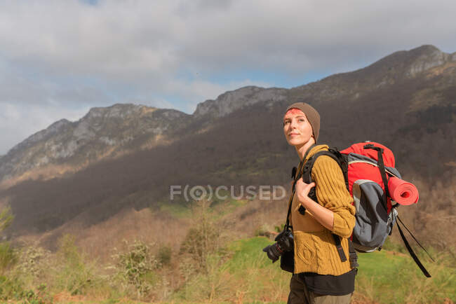 Вид збоку на пустотливу жінку мандрівника з рюкзаком, що йде в горах, дивлячись далеко — стокове фото