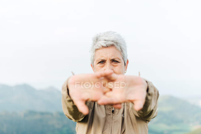 Enfoque suave de la viajera senior estirando los brazos y calentándose durante el viaje en terreno montañoso - foto de stock