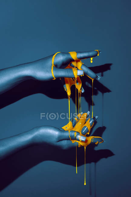 Crop unrecognizable woman showing hand with manicure and bright paint fluids in ultraviolet light on blue background — Stock Photo