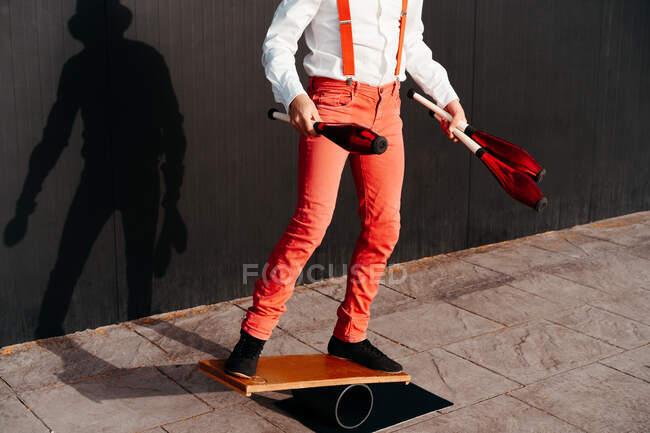 Cropped unrecognizable agile professional young male circus performer juggling clubs and balancing on board — Stock Photo