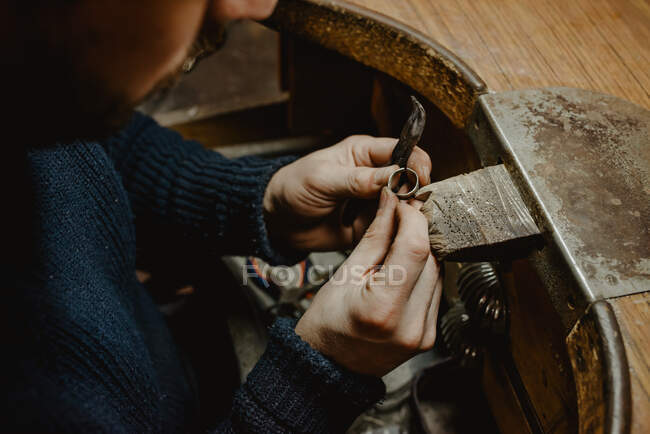 Joalheiro masculino anônimo usando arquivo para moldar anel de metal na bancada na oficina — Fotografia de Stock