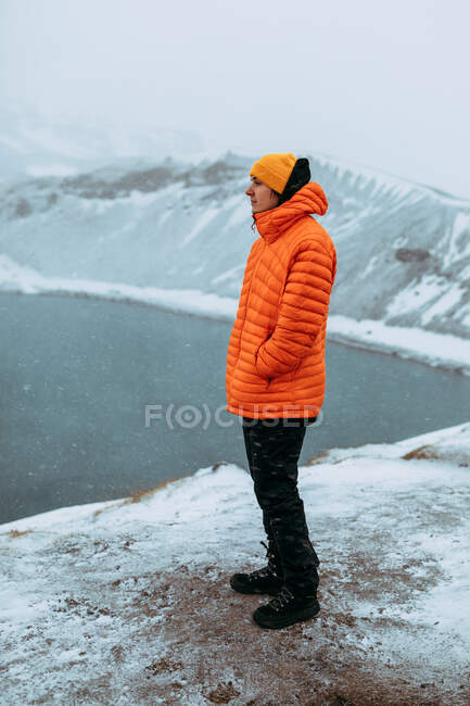 Vista laterale del giovane turista sulla vetta della montagna nella neve guardando l'acqua nella valle — Foto stock