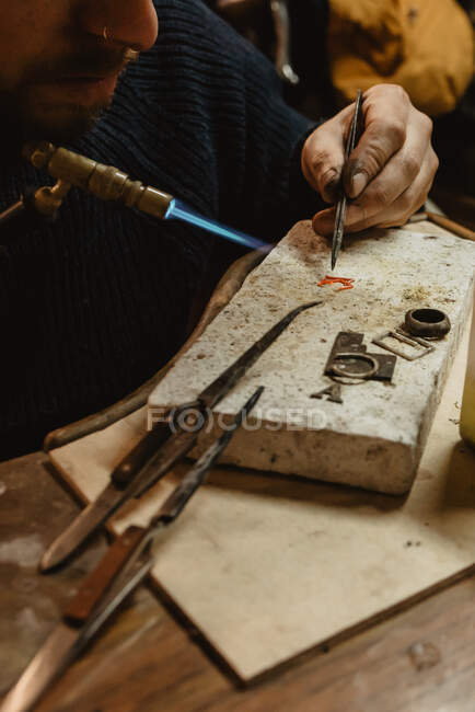 Bearded male goldsmith using tongs while making tiny metal detail on workbench in workshop — Stock Photo
