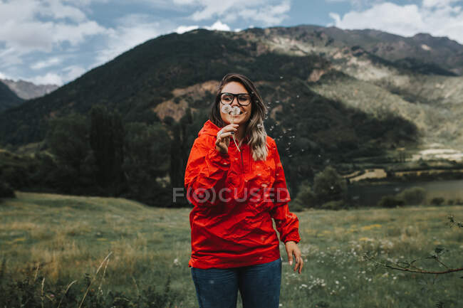 Woman blowing dandelion in forest with mountains — Stock Photo
