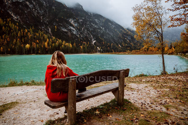 Veduta posteriore di una donna irriconoscibile seduta su una panchina che guarda il lago delle Dolomiti in Italia — Foto stock