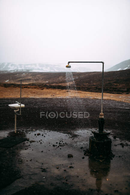Chuveiro retro derramando água no chão perto de colinas de pedra na neve e céu nublado — Fotografia de Stock