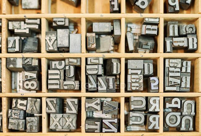 Draufsicht auf eine Reihe schäbiger Buchstaben aus Metall, die in einer Holzkiste in Typografie platziert sind — Stockfoto