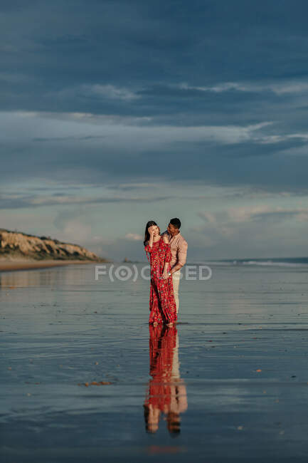 Любящий мужчина обнимает женщину сзади, проводя вместе летний день на берегу моря — стоковое фото