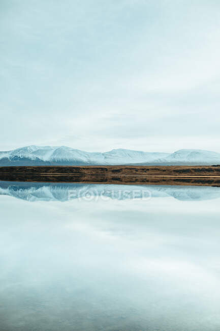 Vue pittoresque de la surface de l'eau près de collines rocheuses étonnantes dans la neige et le ciel bleu — Photo de stock