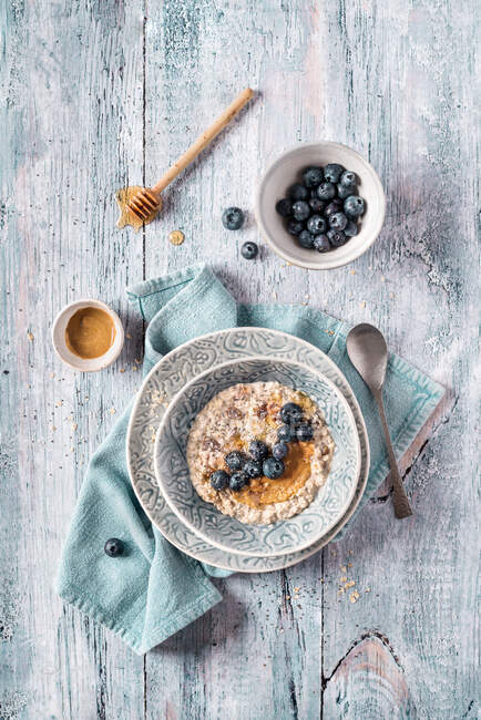 Overhead delizioso porridge di avena fresca durante la notte con mirtilli e panna su asciugamano da cucina su tavolo leggero in legno — Foto stock